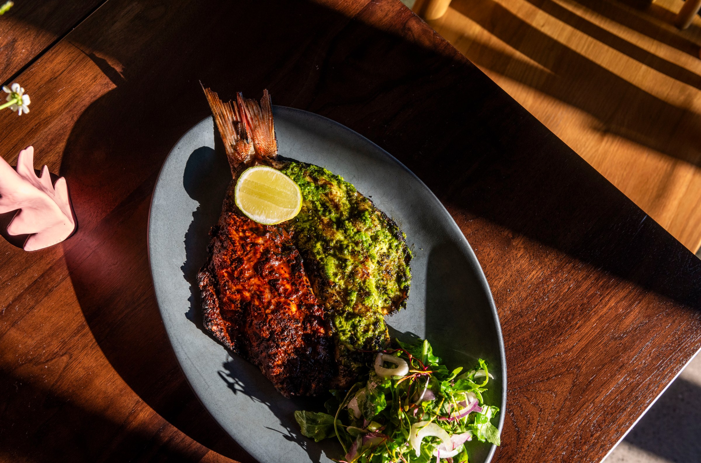 A whole fish at Vecino in Detroit, Michigan set on a blue oval plate on a wood surface.