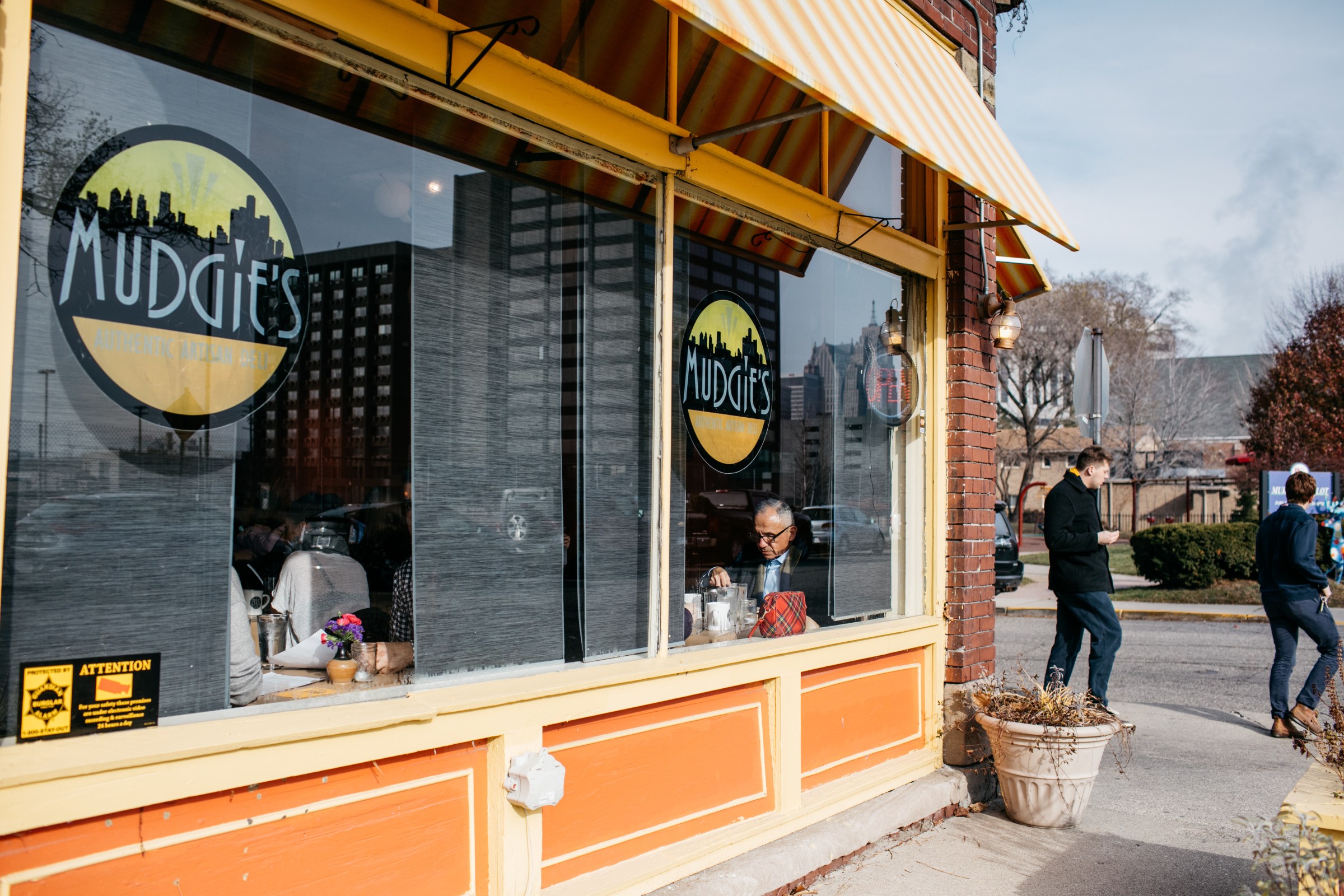 The exterior of Mudgie’s on a sunny day. The building is painted orange with yellow awnings.