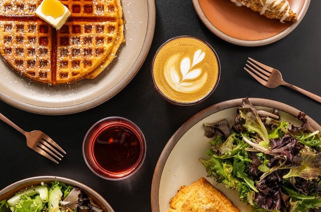 A spread of waffles, salad, lattes, and other accouterments.