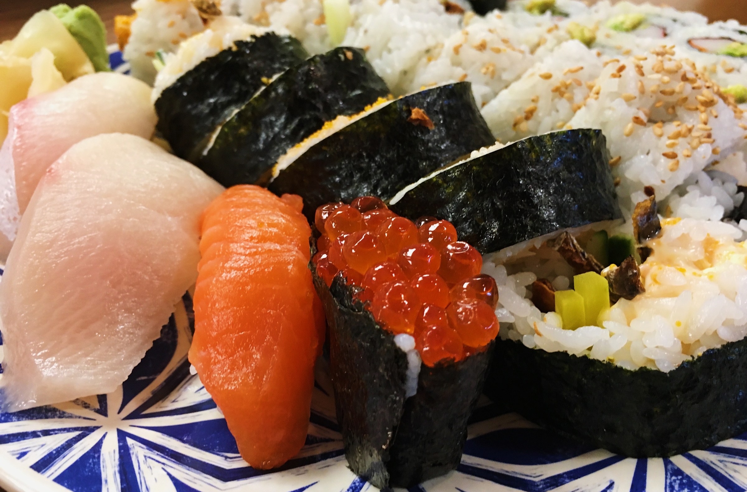 an assortment of nigiri and sushi rolls on a blue and white patterned plate.