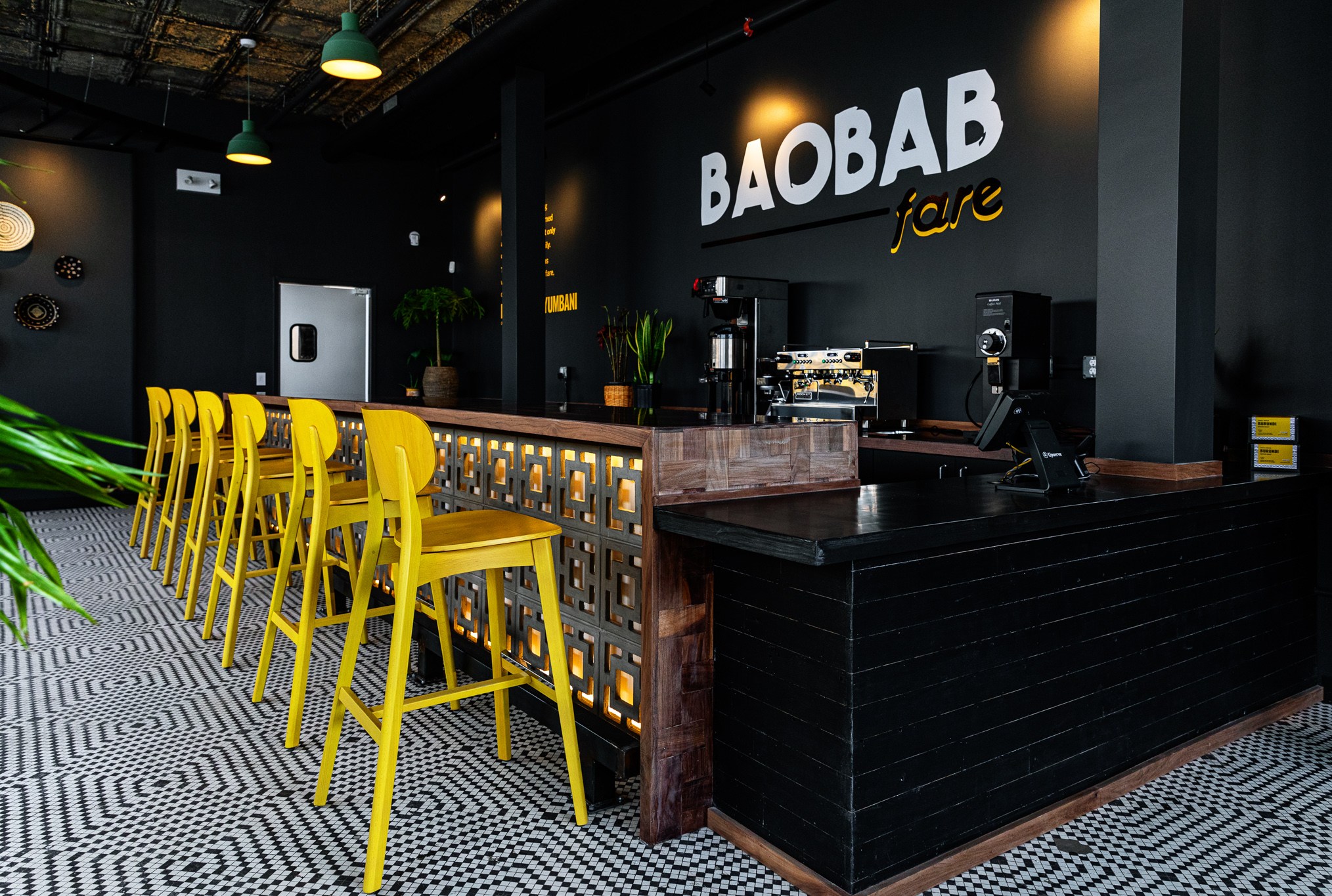 A shot looking down the bar at Baobab Fare with six bright yellow bar stools set atop a blue and white tile floor.