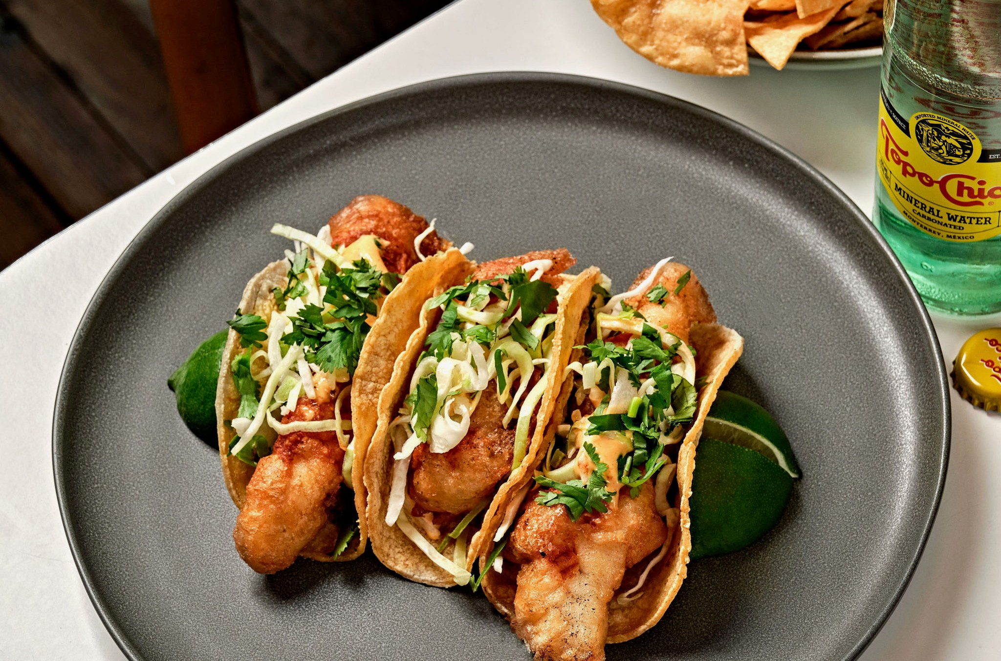 Three fish tacos on a round dark colored plate.
