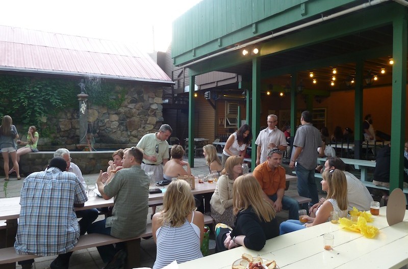 people sit at wooden communal tables on Dominick’s patio