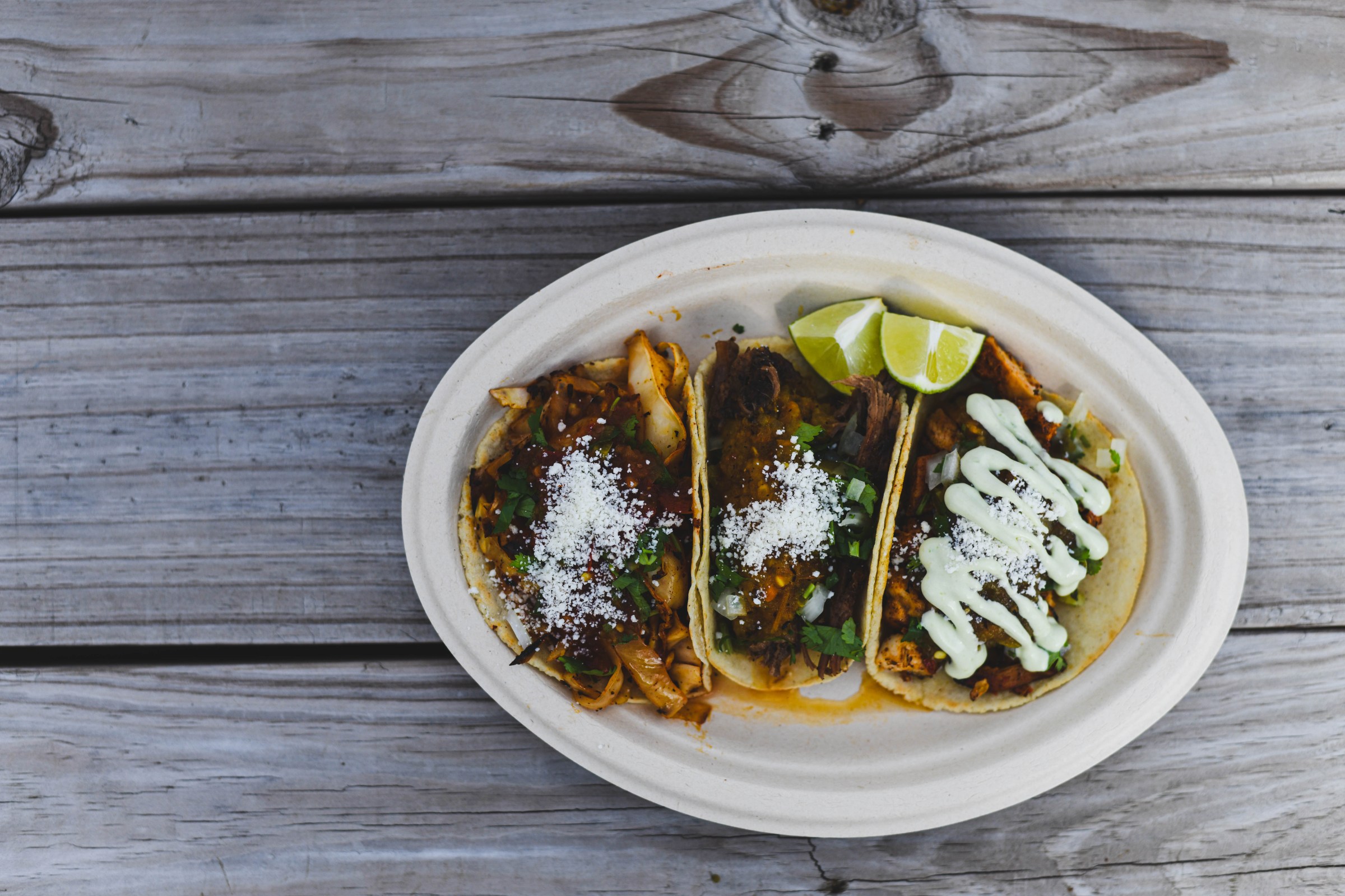 Three tacos on an oval plate on a gray wood surface.