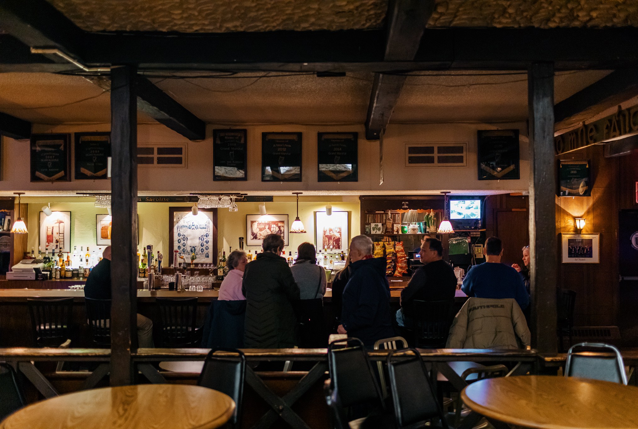 Customers sit along the rail at the bar inside the Gaelic League drinking pints.