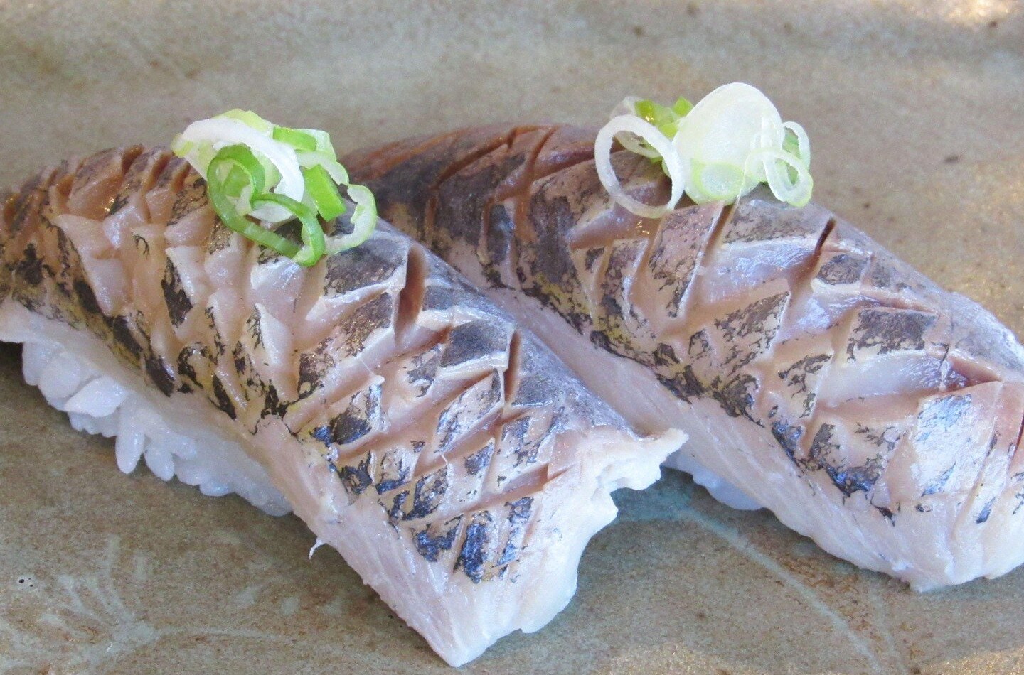Skipjack nigiri that’s sliced along the top into diamonds and dressed with green onion.