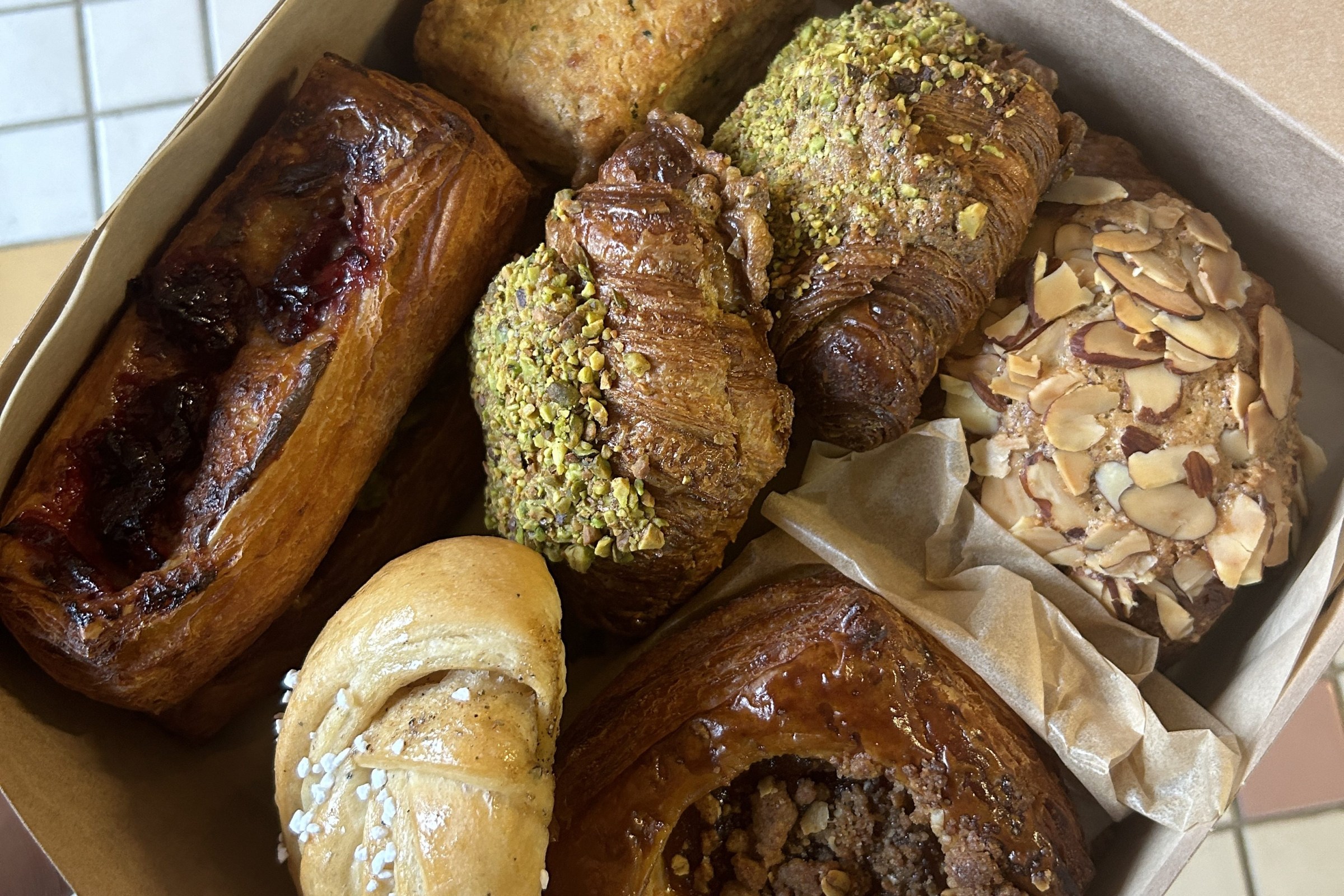 A box of assorted pastries in a square box shot from above with multi-colored tile in the background.