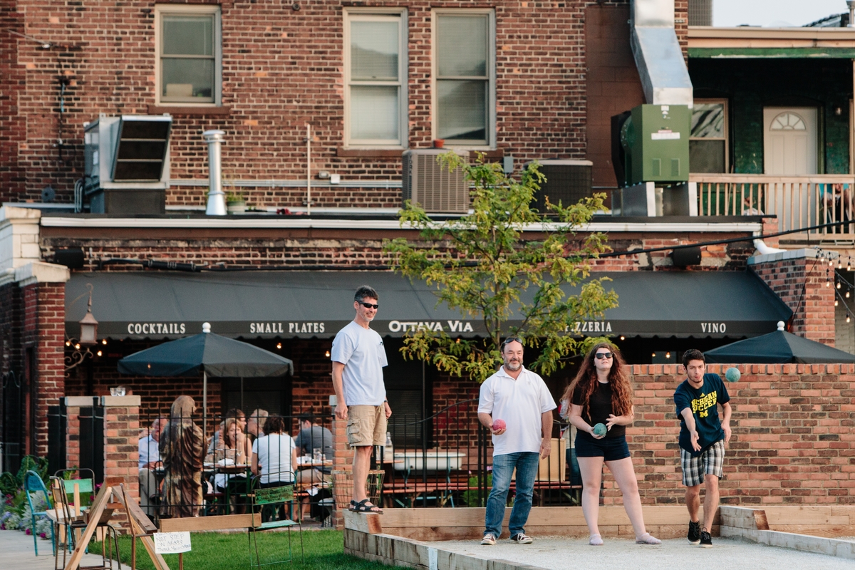 A family plays bocce ball on the patio behind Ottava Via’s brick building.