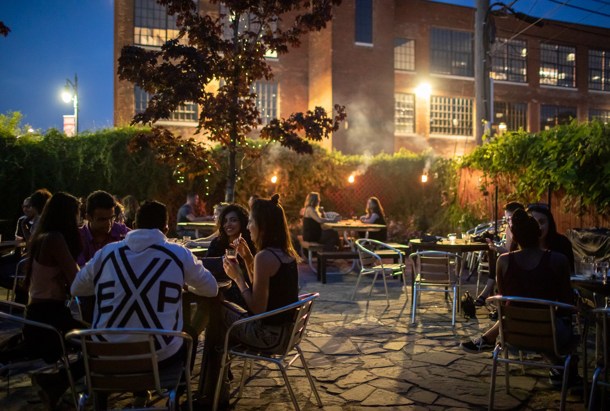 People sit out on the fenced in patio draped in ivy at night.