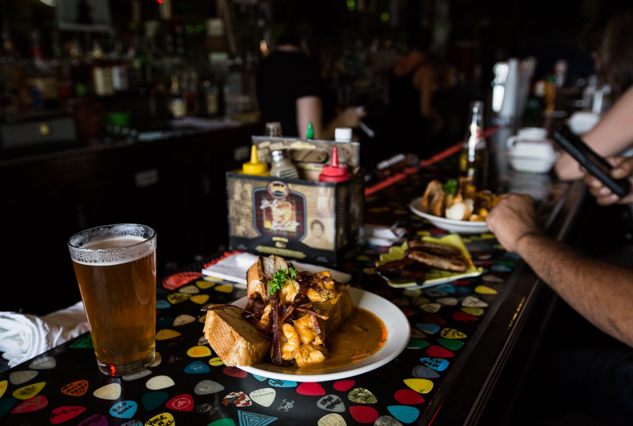 A beer and a plate of food on a bar top embedded with guitar picks.