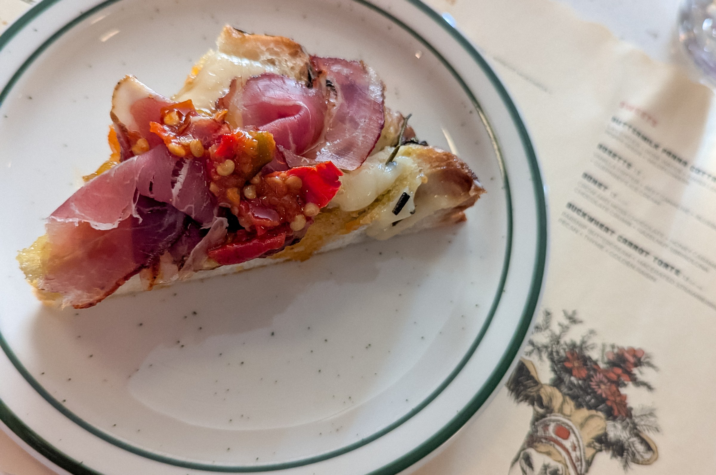 A triangular focaccia slice topped with meat, cheese, and a relish at Alpino.