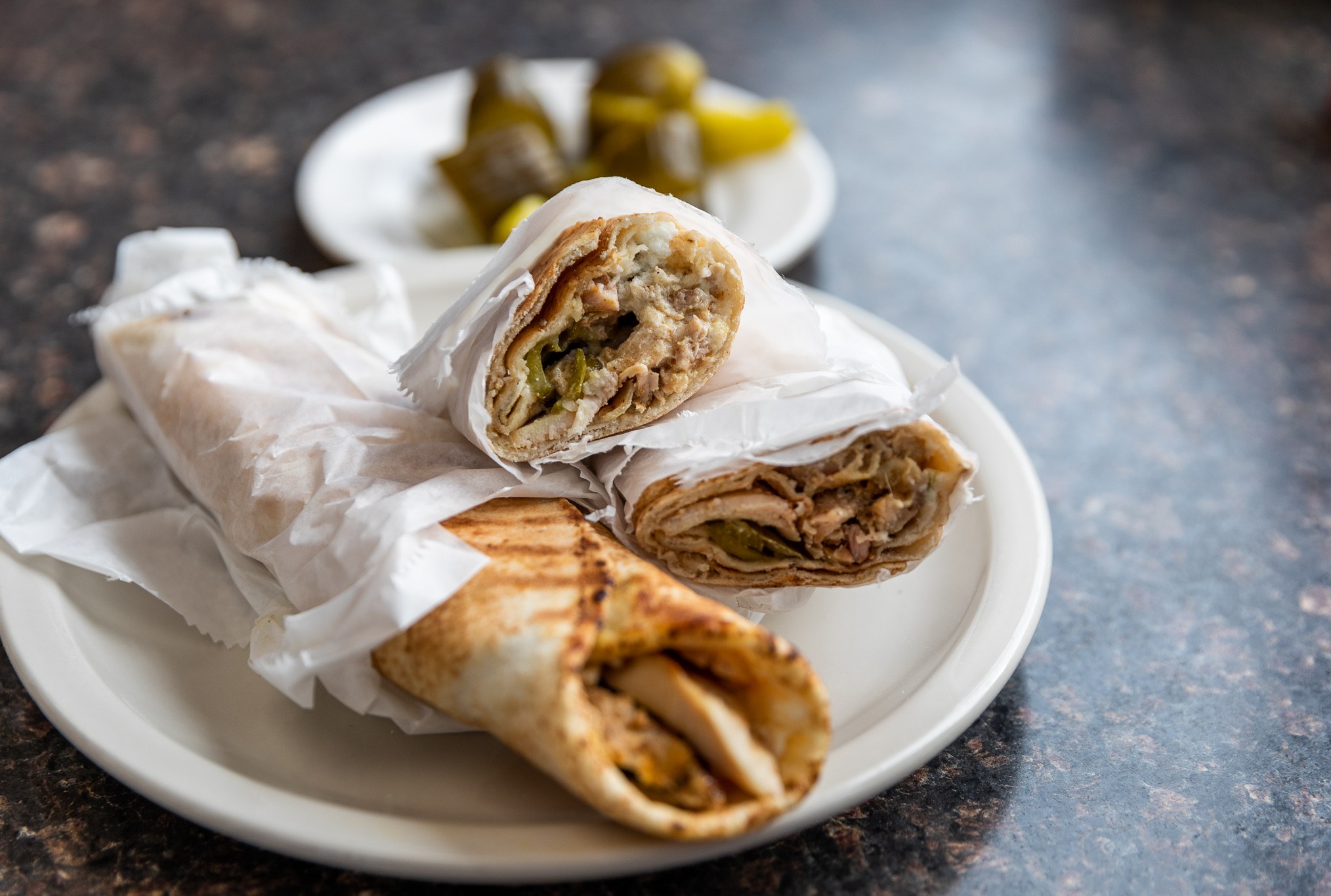 Two chicken shawarma, including one sliced in half, on a plate with a pile of pickled veggies in the background.