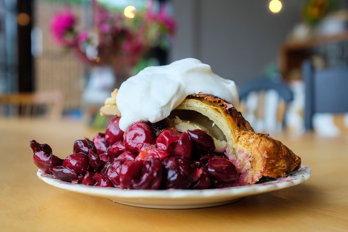 A slice of pie collapsed on a plate with cherry filling falling out and a big dollop of fresh whipped cream on top.