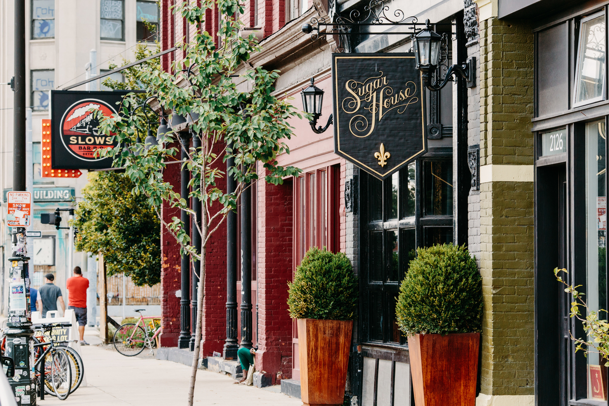 A sign hangs outside the Sugar House on a sunny day looking west down Michigan Avenue.