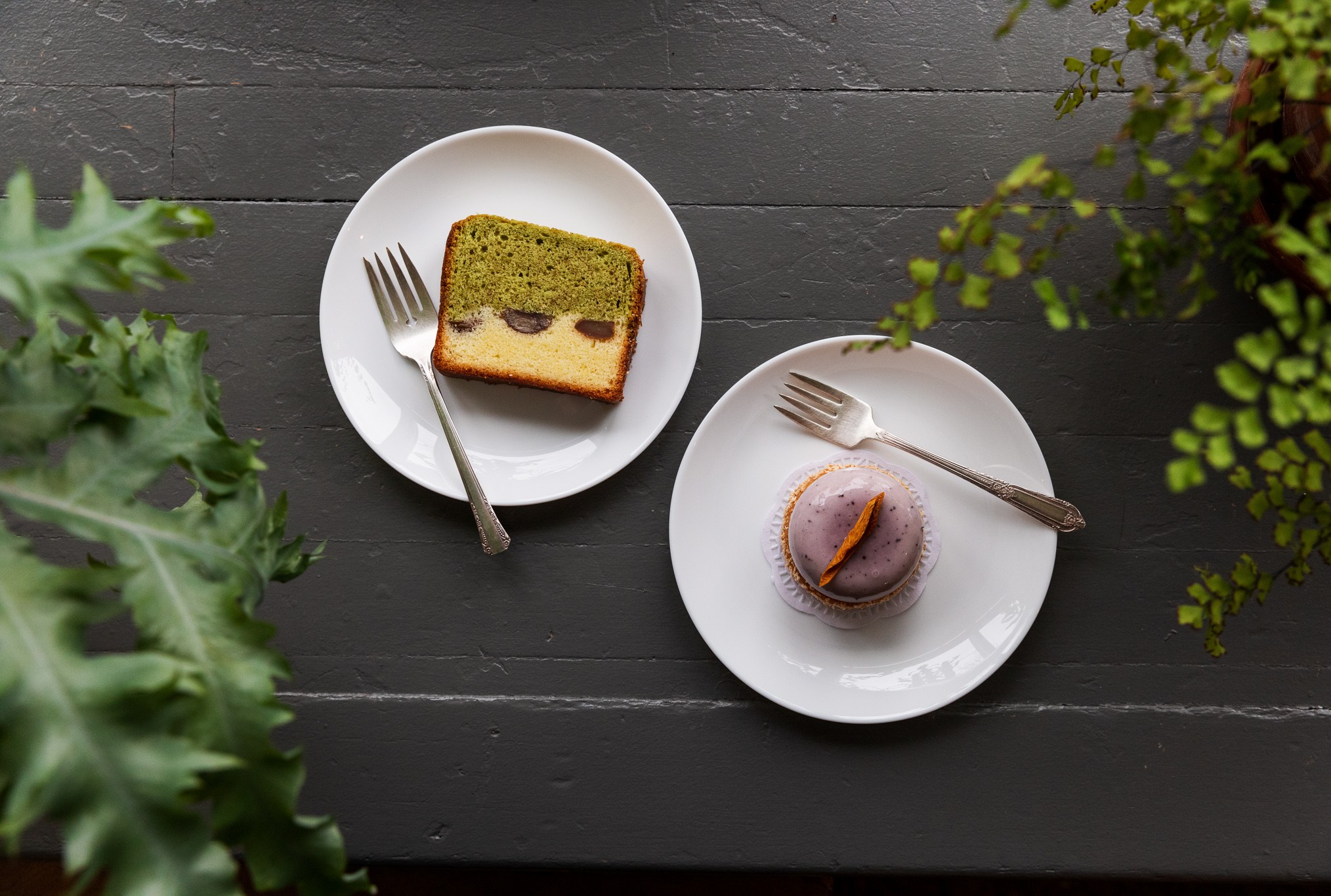 Chestnut cake with white and matcha green marbling and a purple ube pastry surrounded by green plants and delicate forks.