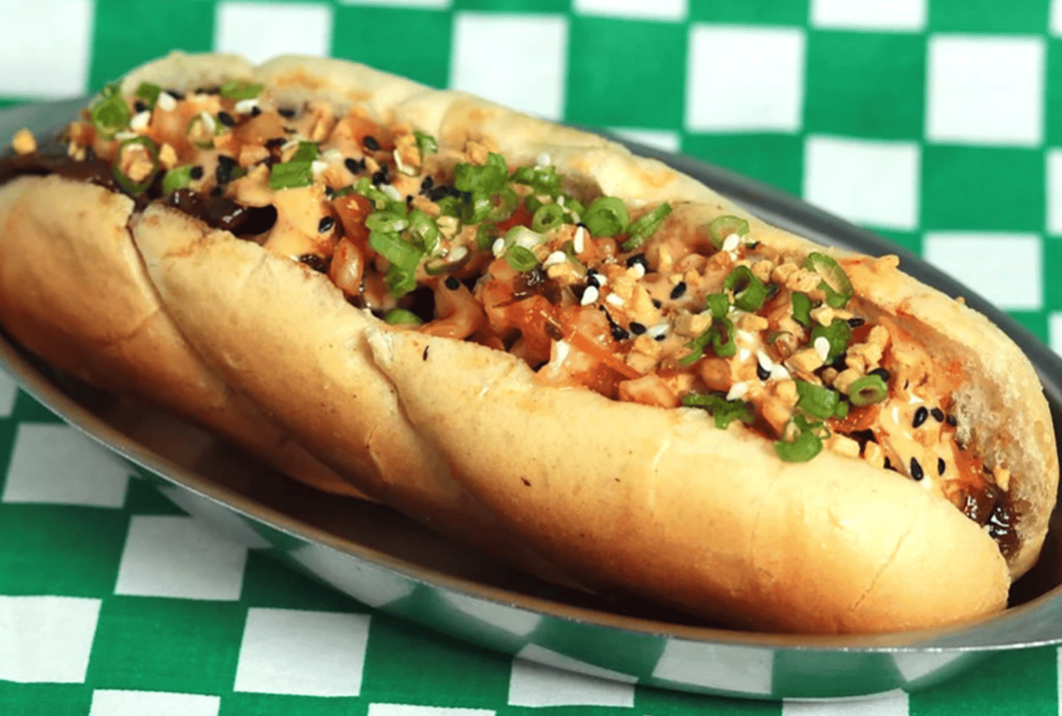 A kimchi dog in a metal dish on green and white checked paper.